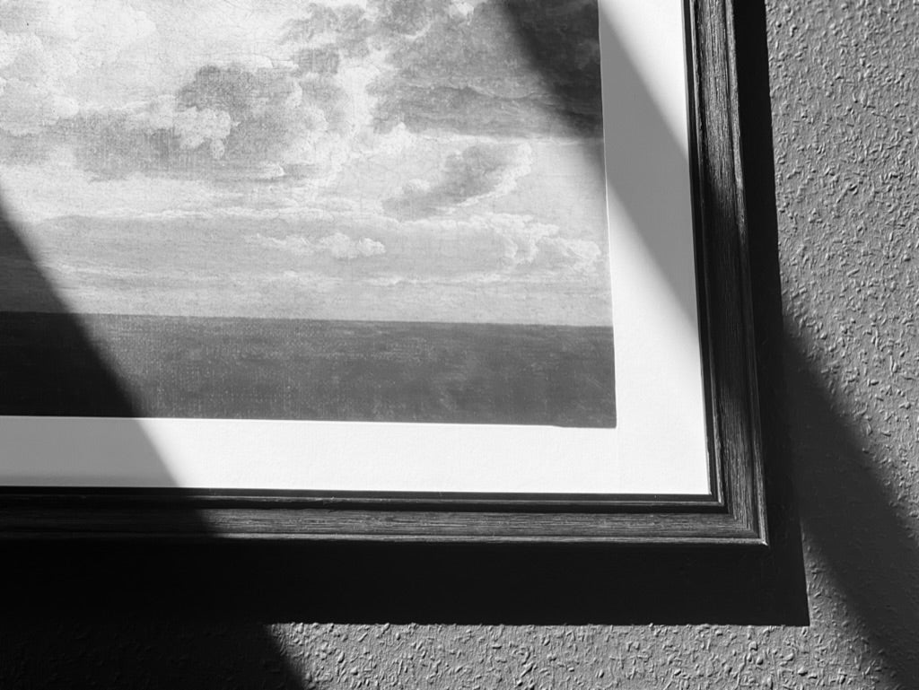 Schwarz-Weiß-Bild eines gerahmten Bildes an der Wand, Motiv ist das Meer mit Wolken auf Ölleinwand